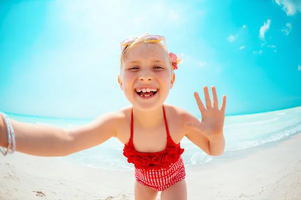 Happy modern child in red beachwear on seacoast taking selfie — Stock Photo, Image