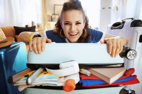 smiling traveller woman trying to close over packed suitcase