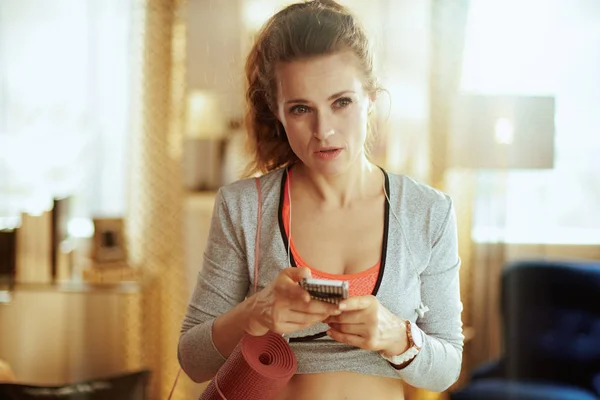 Woman with fitness mat updating a fitness blog via smartphone — Stock Photo, Image