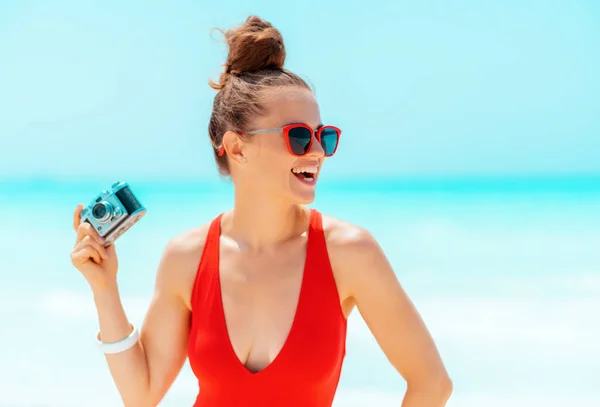 Усміхнена жінка з ретро фотоапаратом дивиться в сторону на пляжі — стокове фото