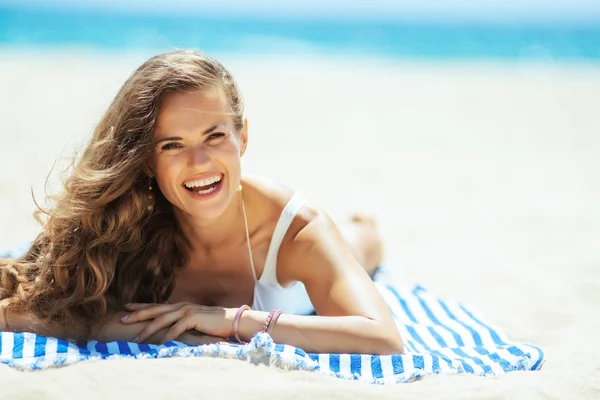 海岸にストライプのタオルの上に横たわる幸せな若い女性 — ストック写真