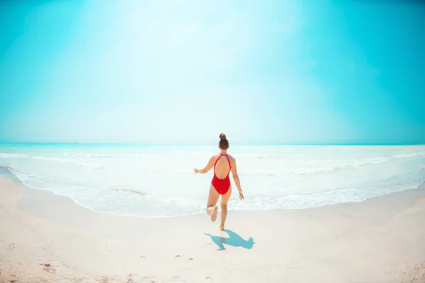 Sett bakifrån ung kvinna i röda strandkläder på Beach Running — Stockfoto