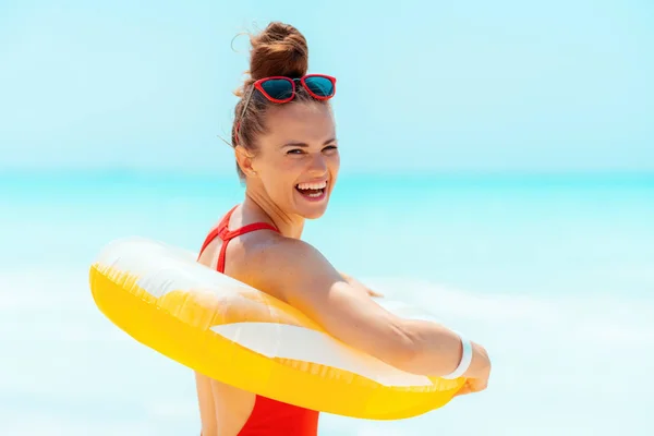 Lachende jonge vrouw op het strand dragen gele opblaasbare reddingsboei — Stockfoto