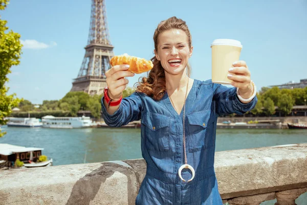 Lycklig ung kvinna visar kopp kaffe och croissant — Stockfoto