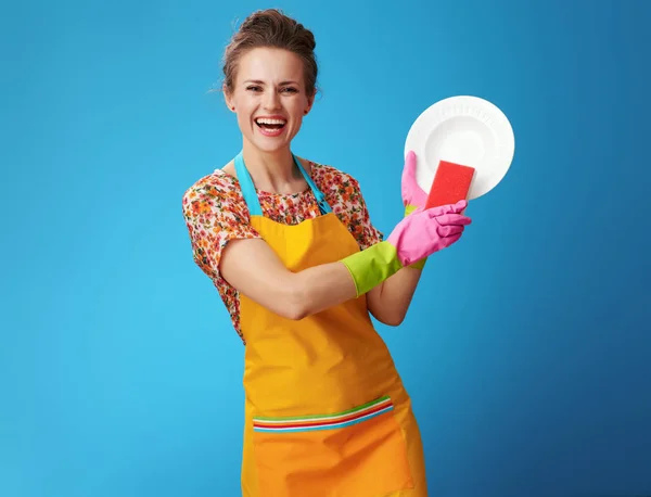 Happy young woman with sponge washing dish on blue — Stock Photo, Image