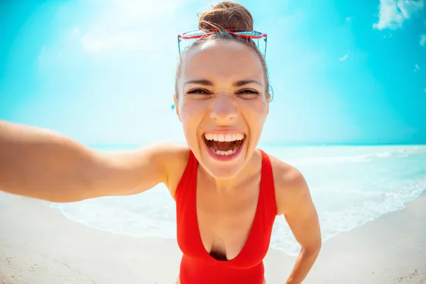 Sorrindo jovem mulher em maiô vermelho na praia tomando selfie — Fotografia de Stock