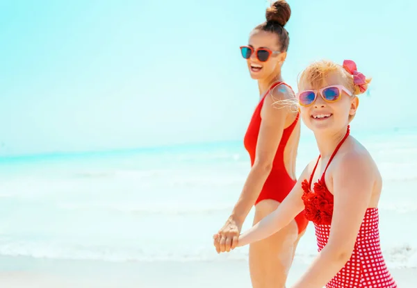 Sonriente joven madre e hijo en traje de baño rojo en la playa caminando —  Fotos de Stock