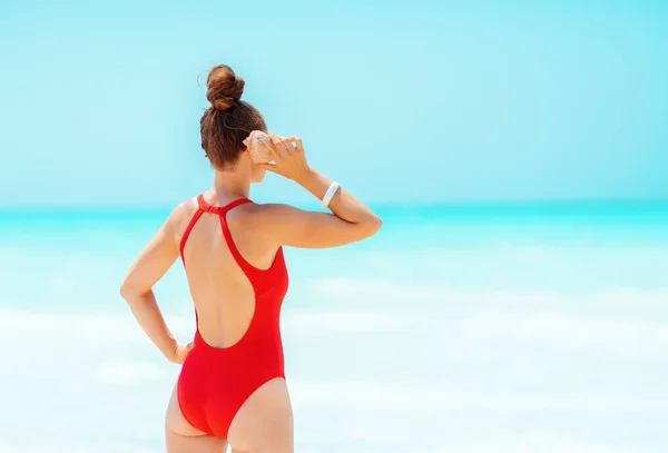 Mujer moderna en la playa escuchando el sonido del océano en concha — Foto de Stock