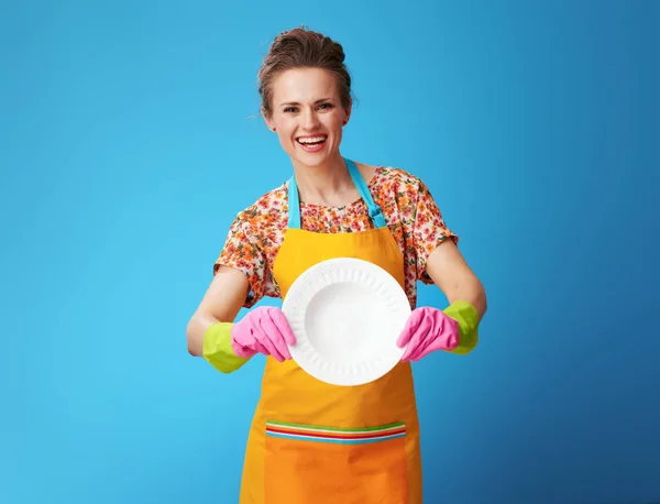 Lachende jonge huisvrouw tonen gewassen plaat op blauw — Stockfoto