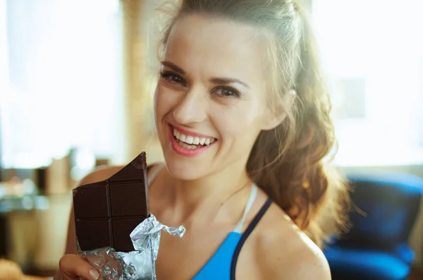 Ευτυχής ταιριάζει γυναίκα στο σύγχρονο σπίτι τρώγοντας σοκολάτα μπαρ — Φωτογραφία Αρχείου