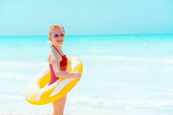 Sorrindo menina moderna com boia inflável amarela na praia — Fotografia de Stock