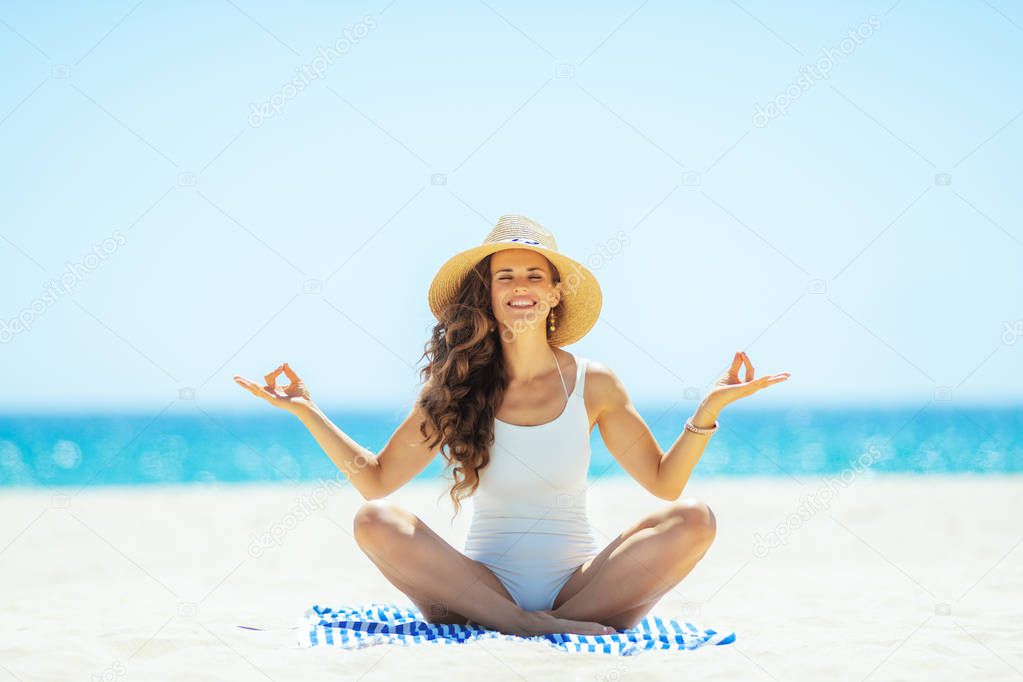 woman doing yoga while sitting on striped towel on seashore