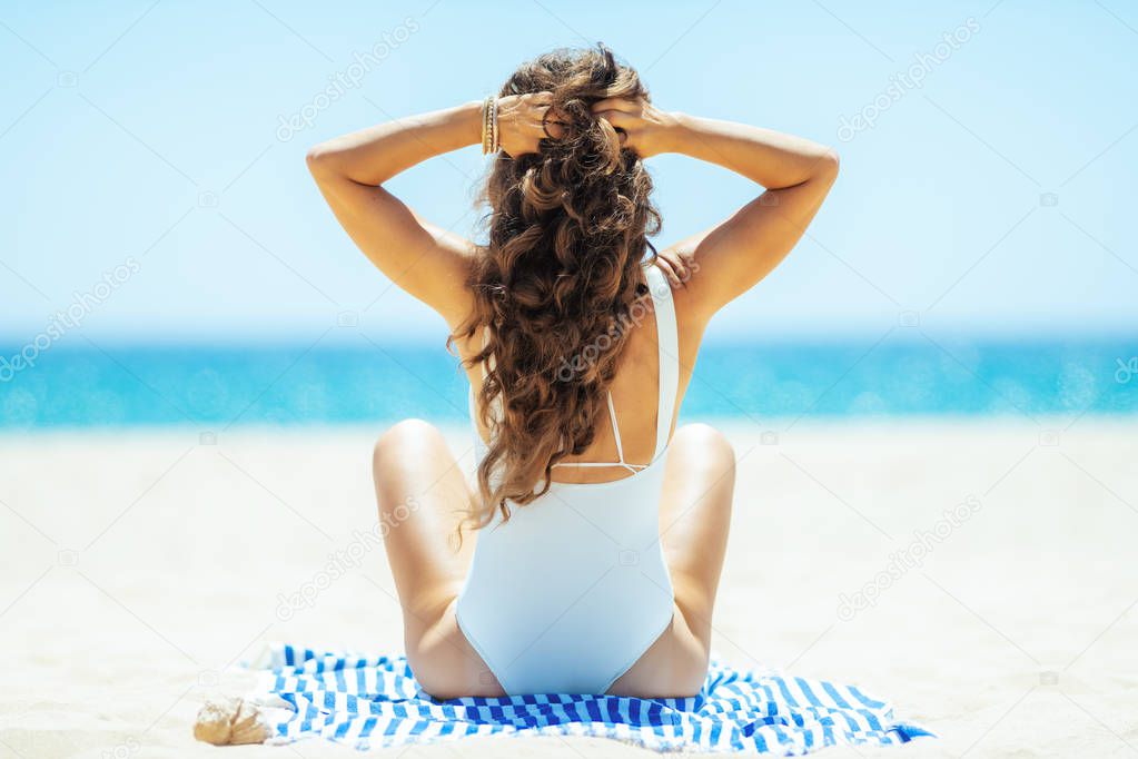 healthy woman on ocean shore siting on striped towel