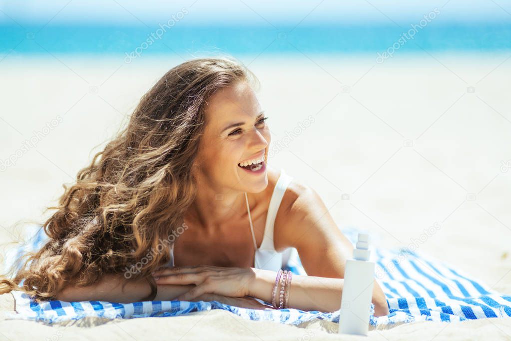 smiling woman with sun screen laying on striped towel