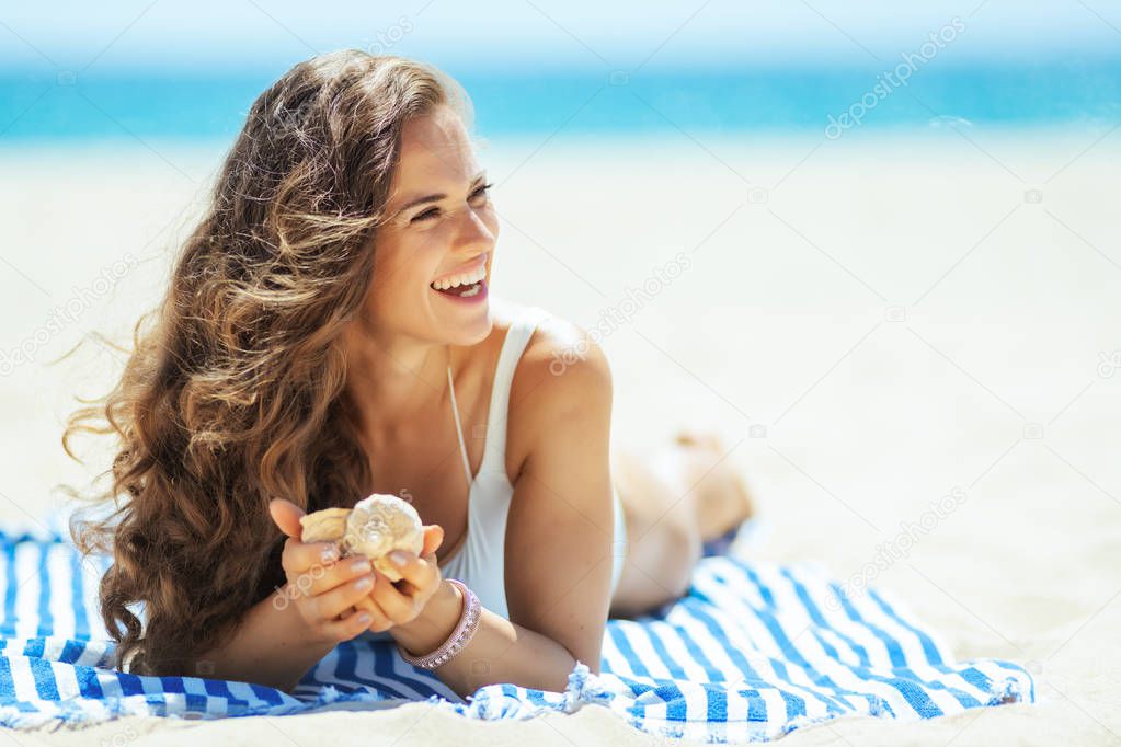 woman with seashell laying on a striped towel and looking aside