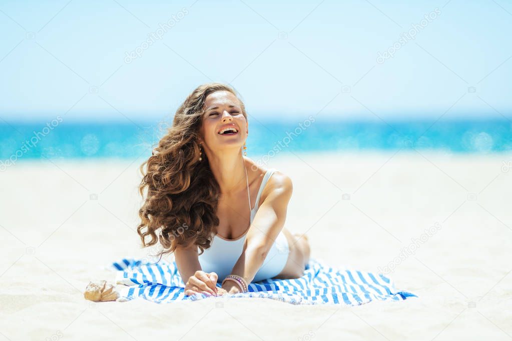 smiling woman on ocean shore lying on striped towel enjoying