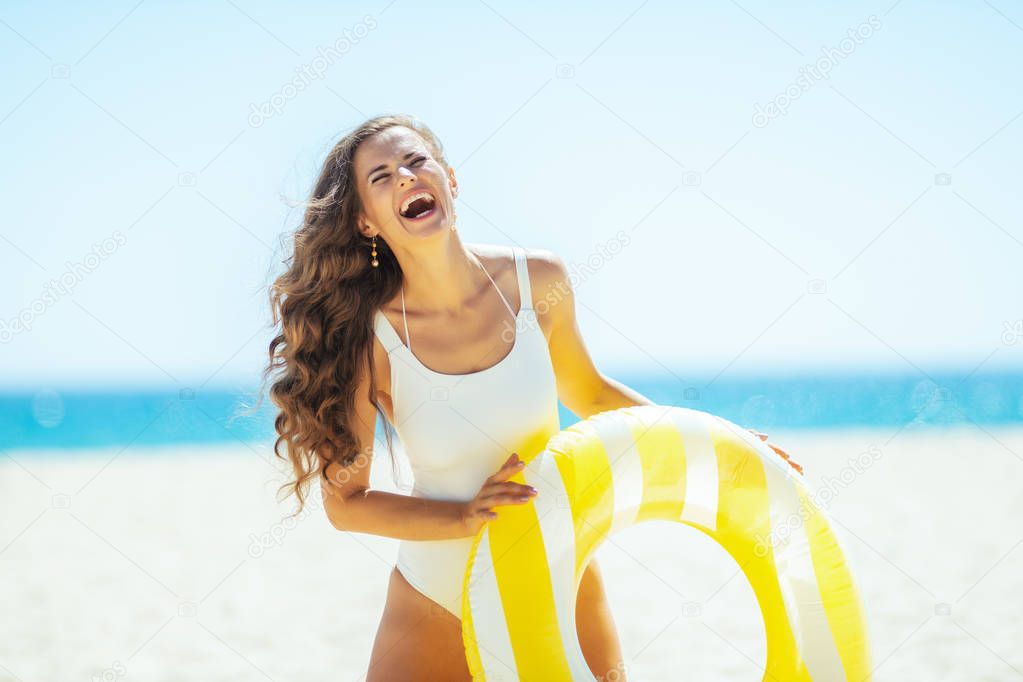 happy woman on ocean coast holding yellow inflatable lifebuoy