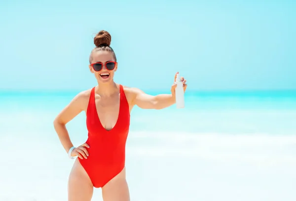 Spf를 보여주는 해변에서 빨간 수영복을 입고 웃고있는 젊은 여성 — 스톡 사진