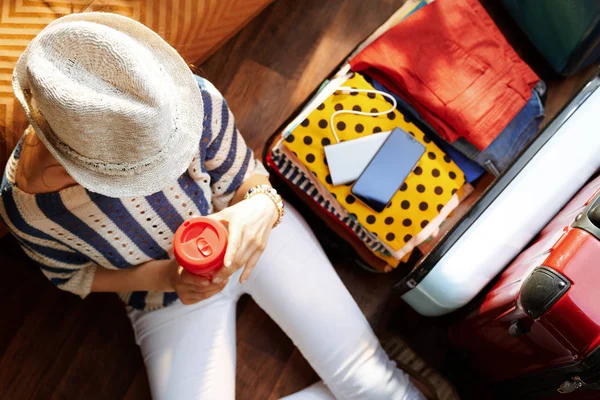 Jeune femme avec tasse de café près de valise de voyage ouverte — Photo