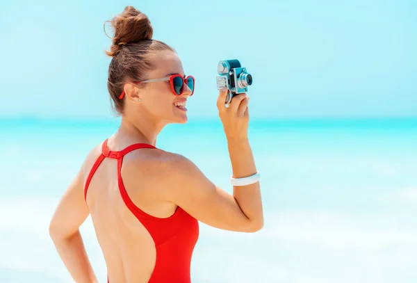 Mujer sonriente tomando fotos con cámara de fotos retro en la costa —  Fotos de Stock
