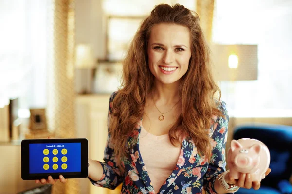 Woman showing tablet PC with smart home application and piggy ba — Stock Photo, Image