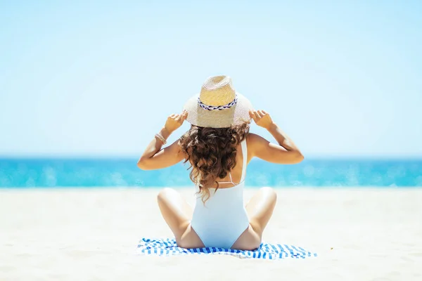 Trendy woman sitting on striped towel on seacoast — Stock Photo, Image