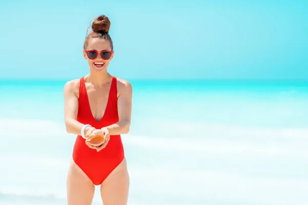 Glückliche junge Frau in roter Bademode am Strand zeigt Muschel — Stockfoto