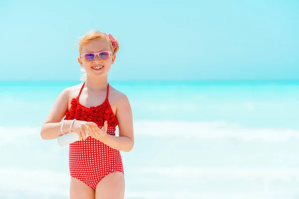 Sonriente niño moderno en la orilla del mar aplicando crema solar —  Fotos de Stock