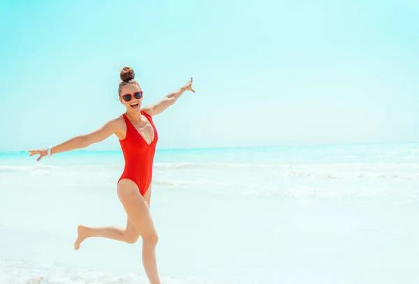 Smiling young woman in red beachwear on beach jogging — Stock Photo, Image