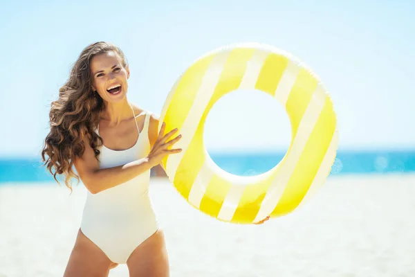 Mujer sonriente en costa del océano sosteniendo boya inflable amarilla —  Fotos de Stock