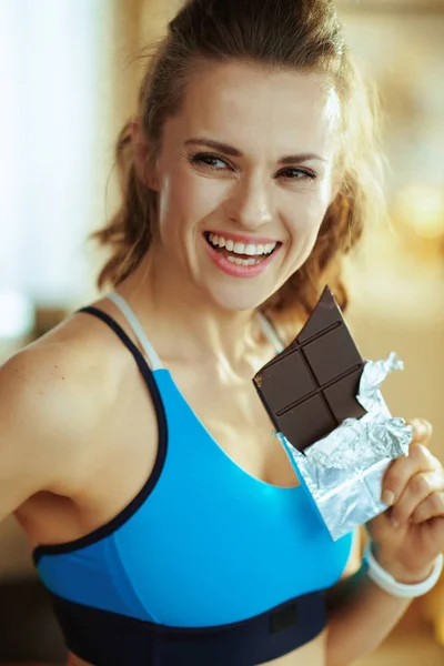 Mulher com barra de chocolate olhando para o lado na sala de estar moderna — Fotografia de Stock