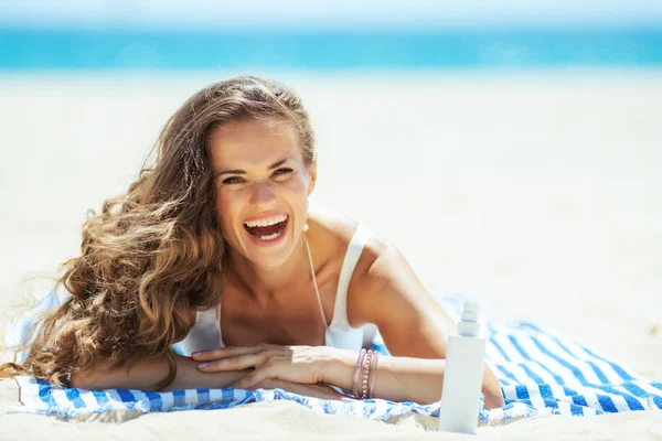 Mujer con crema solar que pone en la toalla rayada en la playa —  Fotos de Stock