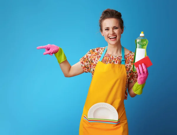 Smiling young housewife with sponge and dish soap on blue — Stock Photo, Image