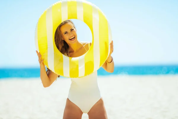 Женщина на берегу моря смотрит сквозь желтый надувной спасательный круг — стоковое фото