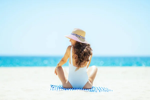 Frau schaut zur Seite, während sie auf gestreiftem Handtuch am Strand sitzt — Stockfoto