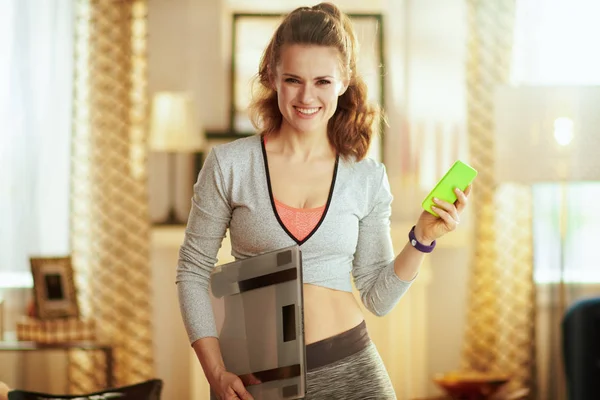 Mujer con peso de seguimiento a escala inteligente en una aplicación en forma en el teléfono —  Fotos de Stock