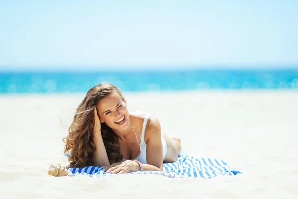 Lächelnde, fitte Frau am Strand liegend auf gestreiftem Handtuch — Stockfoto