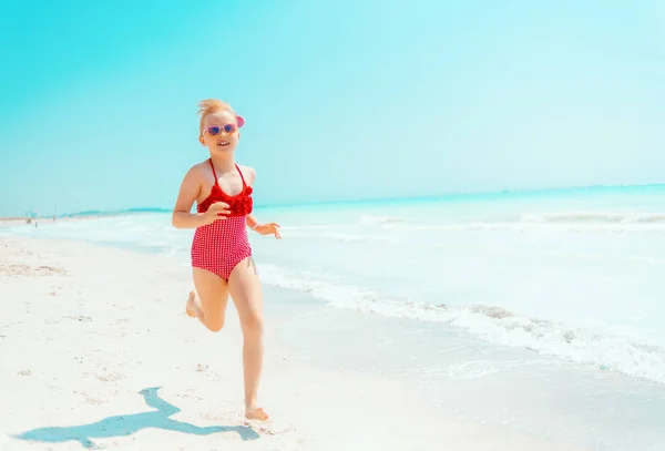 Menina moderna em maiô vermelho na praia correndo — Fotografia de Stock