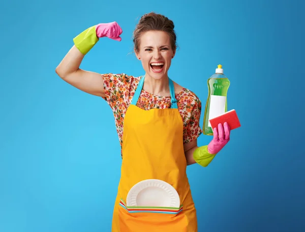 Housewife with sponge and dish soap showing biceps on blue — Stock Photo, Image