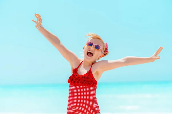Lächelndes modernes Kind in roter Bademode am Strand jubelt — Stockfoto