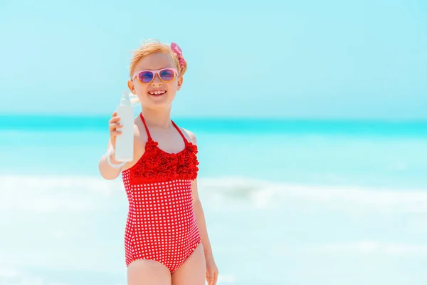 Sorridente ragazza moderna sulla costa mostrando lozione abbronzatura — Foto Stock