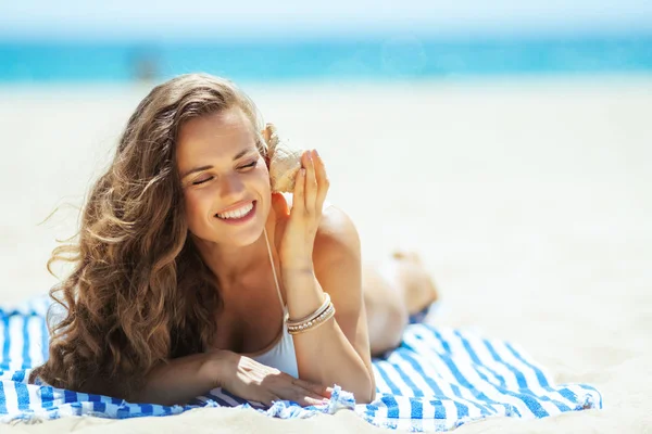 Woman laying on a striped towel and listening to seashell Stock Picture