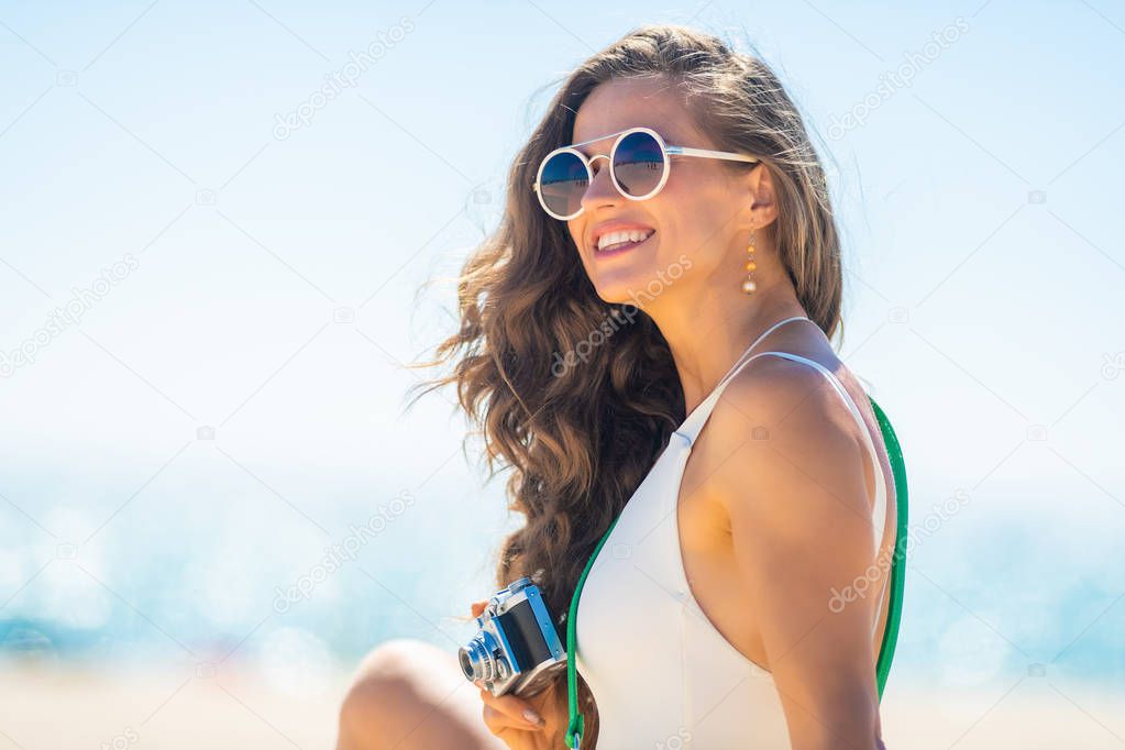 woman with retro photo camera looking into distance on beach