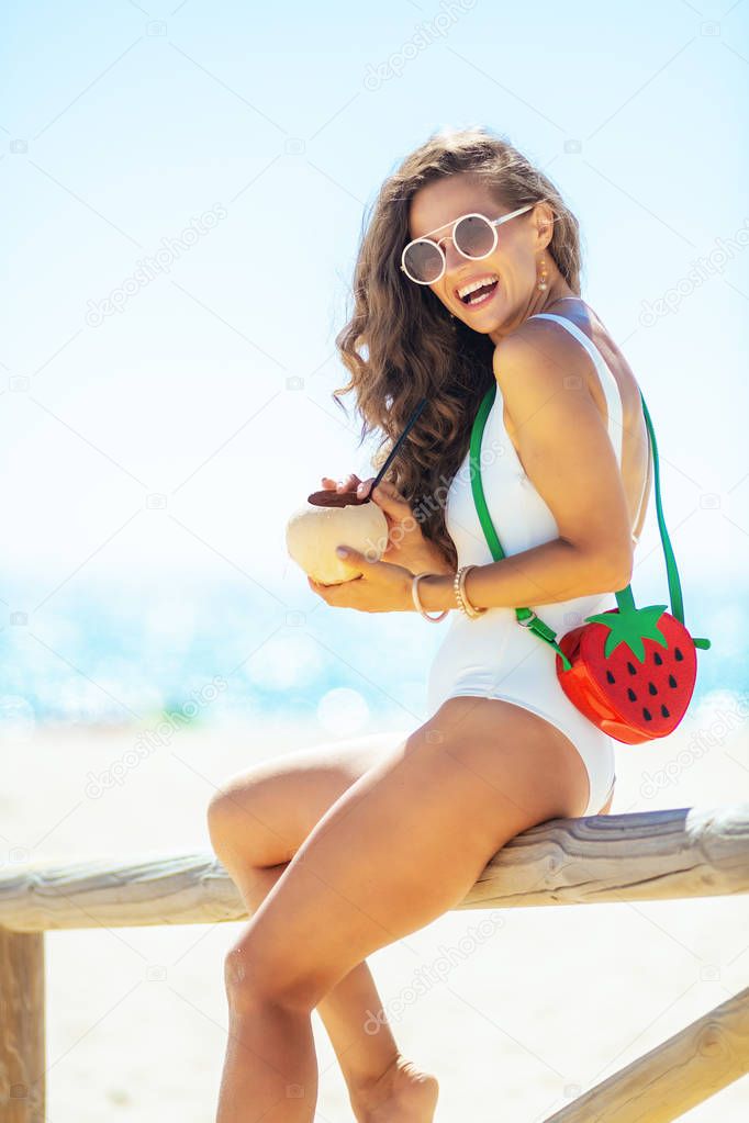 woman sitting on wooden fence with coconut on ocean shore