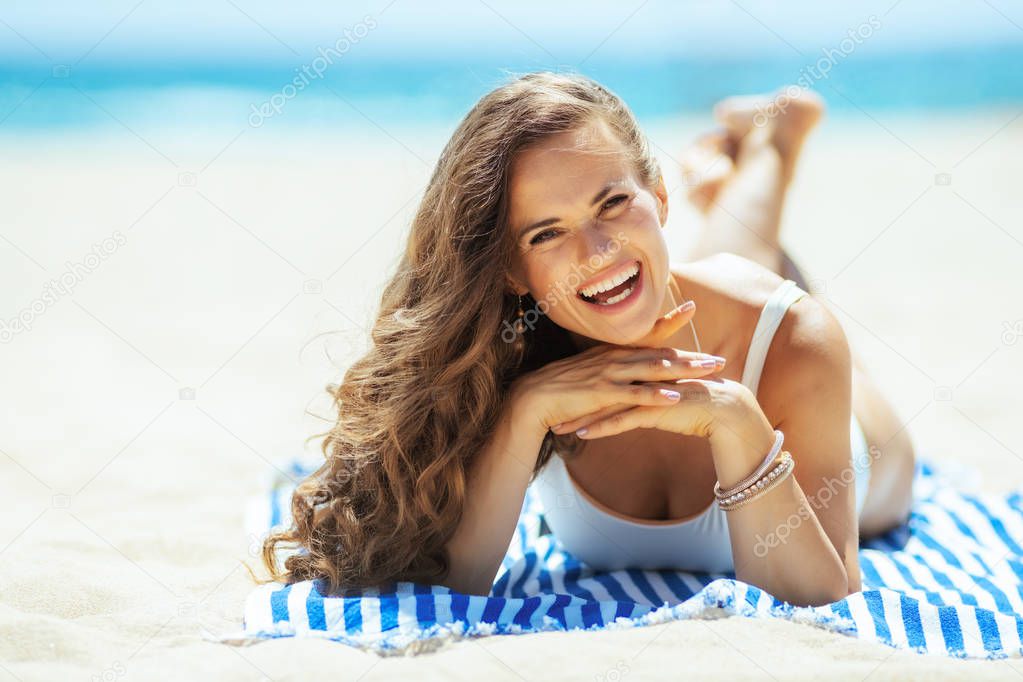smiling young woman laying on striped towel on seacoast