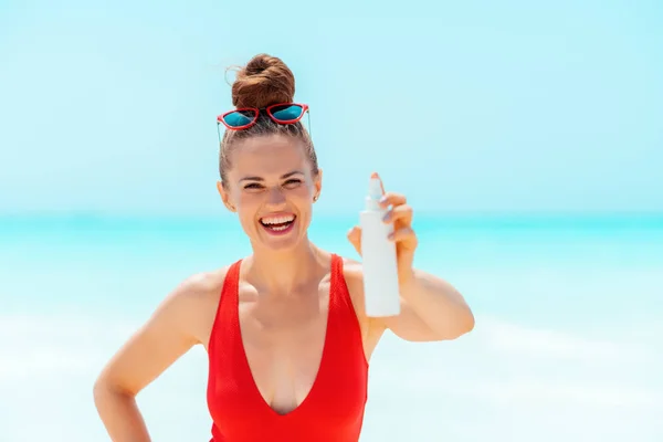 Smiling young woman on seacoast showing sun cream — Stock Photo, Image