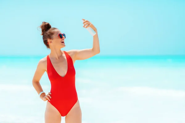 Smiling young woman on seashore applying suntan lotion — Stock Photo, Image