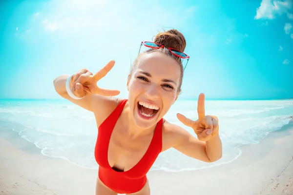 Feliz jovem mulher em roupa de banho vermelha na praia mostrando vitória — Fotografia de Stock