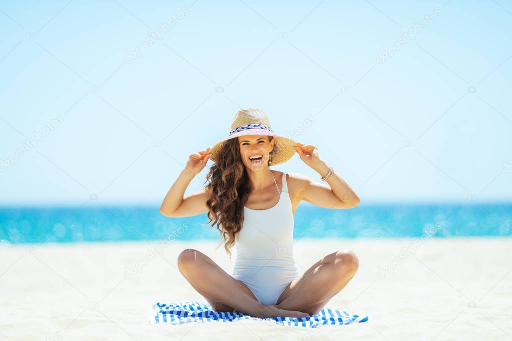 happy young woman sitting on striped towel on seacoast