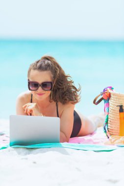 zarif 40 yaşındaki kadın uzun kıvırcık saçlı zarif siyah mayo beyaz bir plajda sosyal medyada paylaşım.